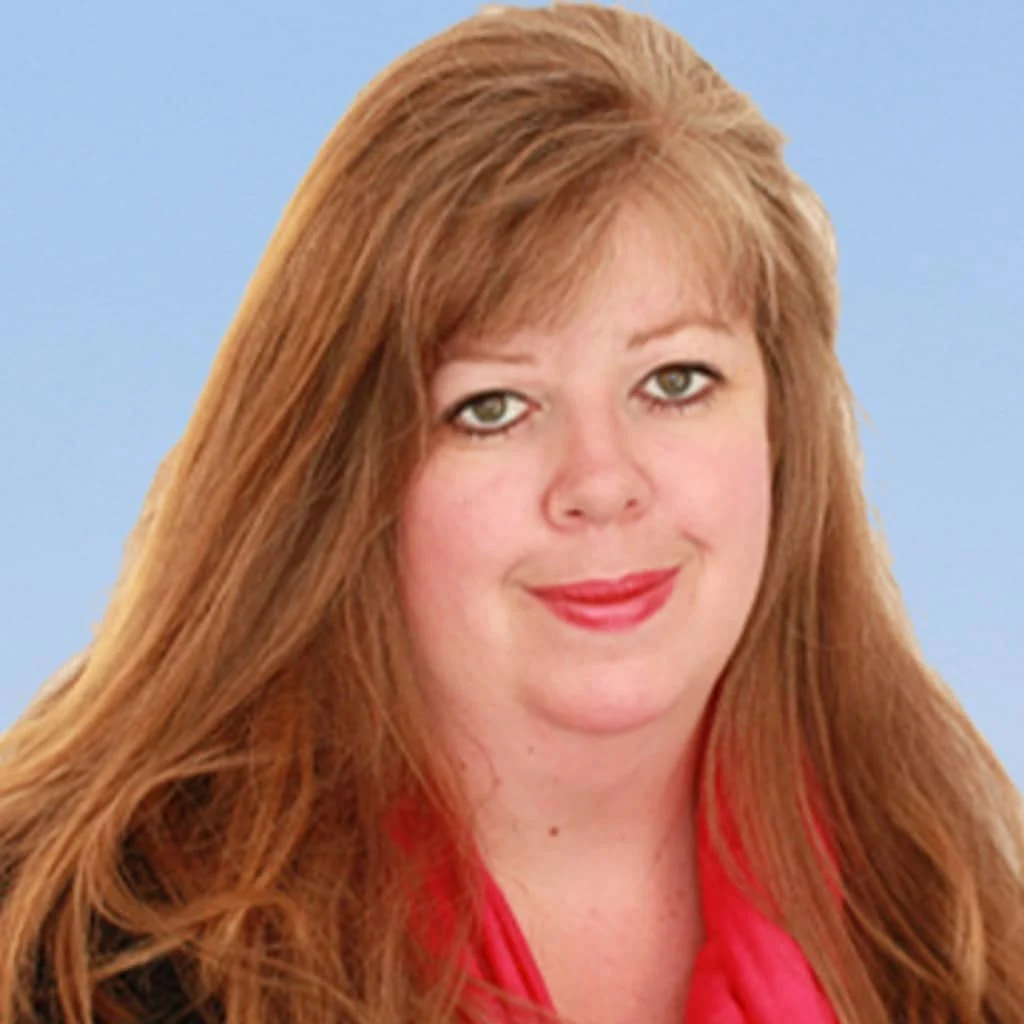 A woman with long, light brown hair and fair skin is smiling slightly. She is wearing a pink scarf and a dark top, posed in front of a plain light blue background.